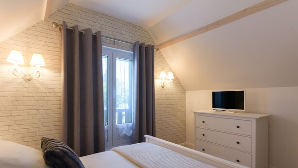 A bedroom with a bed, a dresser, a television, and a window with curtains.
