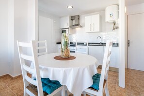 A modern kitchen with white cabinets, a round table with teal cushions, and a decorative vase.