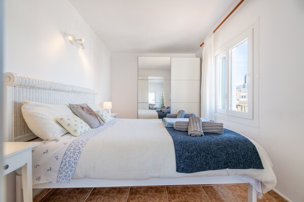 A modern hotel room with a large bed, a bedside table, a mirror, and a window with a city view.