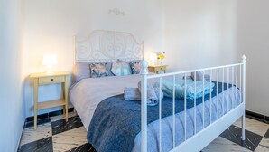 Een net opgemaakt bed met een hoofdbord, twee nachtkastjes met lampen en een kamer met een vloerkleed.