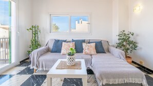 Een moderne woonkamer met een bank, twee ramen, een potplant en een salontafel.