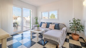 Een woonkamer met een bank, een bijzettafeltje, een potplant en een uitzicht door een schuifdeur op een balkon.