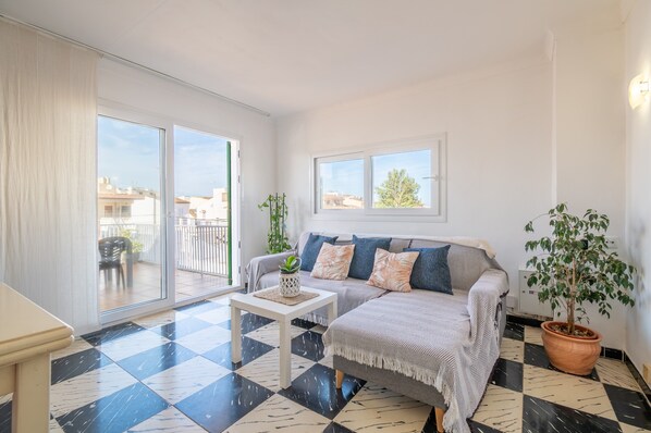 A living room with a sofa, a coffee table, a potted plant, and a view through a sliding door to an outdoor balcony.