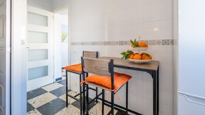 Een keuken met een betegelde spatwand, een houten tafel, twee stoelen met oranje kussens en een fruitmand op de tafel.