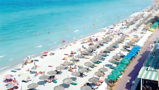 Een strand met rijen parasols en ligbedden, een zandstrand en de zee.