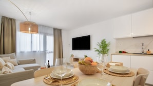 A modern living room with a dining area, a flat-screen TV, and a kitchen with white cabinets.
