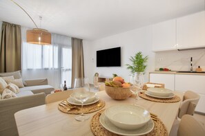 En moderne stue med spiseområde, et fladskærms-tv og et køkken med hvide skabe.