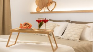 A bed with a wooden bedside table holding a plate of fruit and two glasses of red beverage.
