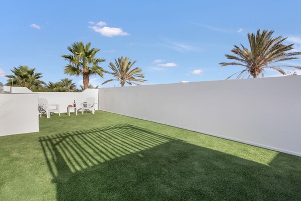 A rooftop patio with artificial grass, white walls, and palm trees.