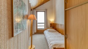 A bedroom with a wooden ceiling, a bed, a nightstand with a lamp, a wall-mounted artwork, and a door.