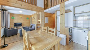 A wooden interior with a dining table, sofas, a TV, and a kitchen area.
