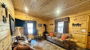 A cozy log cabin interior with a sofa, armchair, and a fireplace.