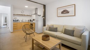 A modern living room with a sofa, a wicker chair, a wooden coffee table, and a kitchen in the background. - Vacation Home 'Casa Fela' with Wi-Fi (Caleta de Famara)