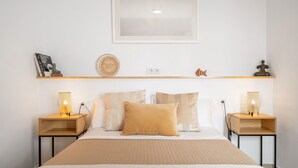 A neatly arranged hotel room with a bed, two bedside tables, a wall-mounted shelf, and a framed picture above the bed. - Vacation Home 'Casa Fela' with Wi-Fi (Caleta de Famara)