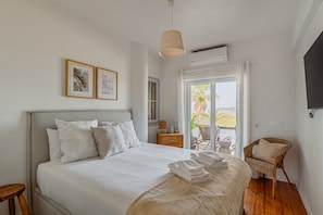 A bedroom with a bed, a chair, a bedside table, and a window.