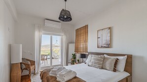 Et soveværelse med seng, sengebord, lampe, stol, vindue med gardiner og udsigt til det fri.