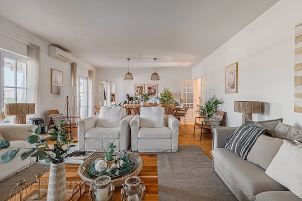 A spacious living room with a sofa, chairs, a dining area, and a kitchen in the background.