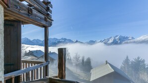 A wooden balcony with a view of snow-covered mountains and a house in the distance.
