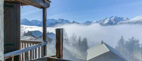 A wooden balcony with a view of snow-covered mountains and a house in the distance.