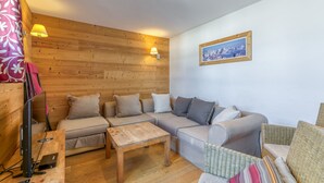 A cozy living room with a wooden wall, a sofa set, a coffee table, a TV, and a framed picture on the wall.