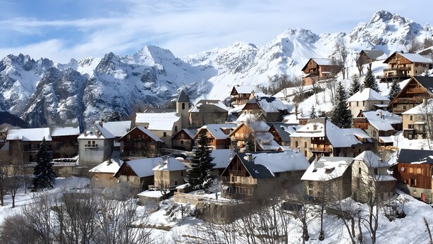 A snow-covered village with traditional wooden houses, a church, and mountains in the background.