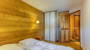 A room with wooden panel walls, a bed with white bedding, a small bedside table, and a sliding door.