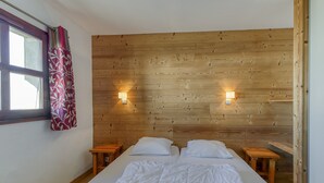 Une chambre avec des murs recouverts de panneaux de bois, deux tables de chevet, un lit avec une literie blanche, une fenêtre avec un rideau et des lampes fixées au mur.