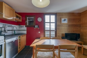 Une cuisine avec des meubles de rangement en bois, une table à manger, des chaises, une horloge et une fenêtre donnant sur un beau paysage.