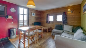 Une pièce chaleureuse avec un mur en bois, une table à manger avec des chaises, un canapé, une horloge et une fenêtre avec des rideaux.