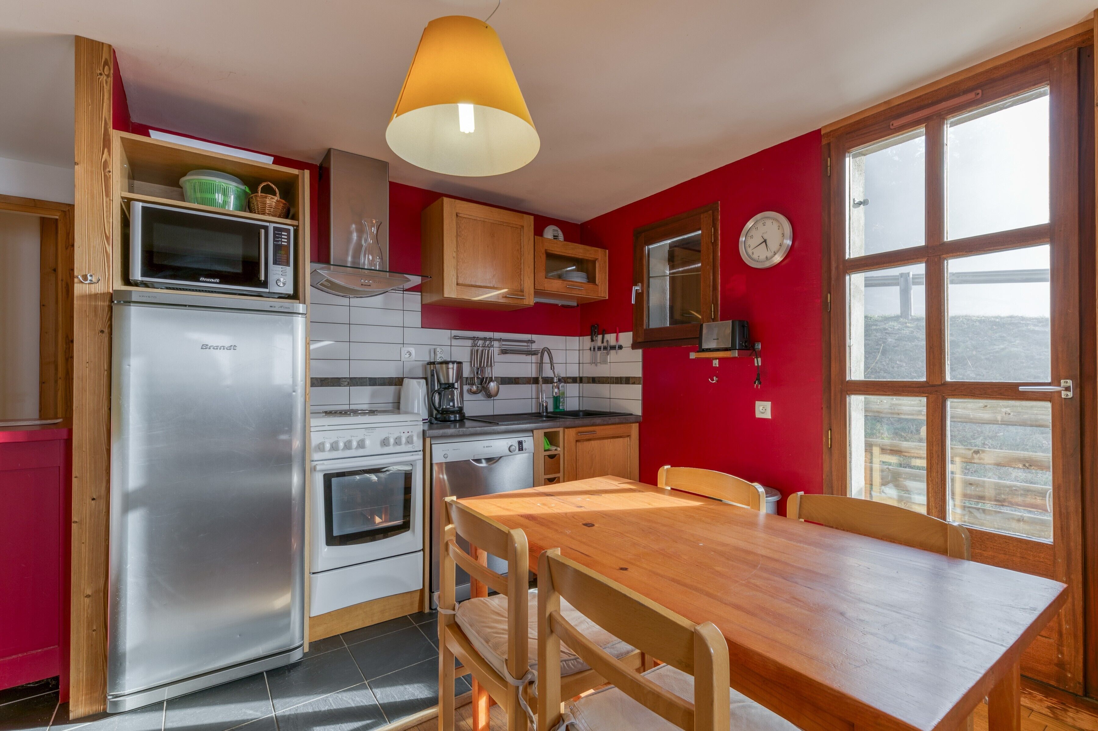 Una cucina con un frigorifero Brandt, un forno a microonde, un fornello e un tavolo da pranzo in legno.