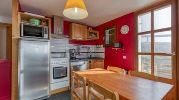 Una cucina con un frigorifero Brandt, un forno a microonde, un fornello e un tavolo da pranzo in legno.