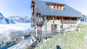 Un chalet de montagne avec une façade en bois, un balcon et une vue sur des montagnes enneigées.