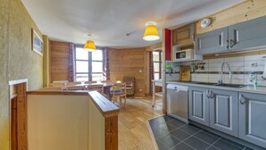 A kitchen with grey cabinets, a microwave, and a sink. There is a wooden dining table with chairs. - Apartment 'Regain 1' with Mountain View and Balcony (Villard-Reculas)