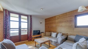 A living room with a sofa set, a coffee table, a TV, and a wooden wall. - Apartment 'Regain 1' with Mountain View and Balcony (Villard-Reculas)