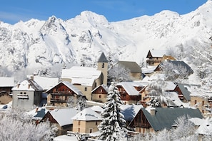A snow-covered mountain village with wooden buildings, a church, and a prominent mountain peak in the background.