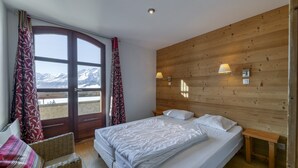 Quarto com cama, cadeira, parede de madeira e janela com cortinas.