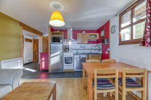 Cocina compacta con electrodomésticos modernos, comedor con mobiliario de madera e iluminación colgante brillante.