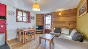 Uma sala de estar com piso de madeira, um sofá, uma televisão, uma mesa de jantar com cadeiras e um abajur.