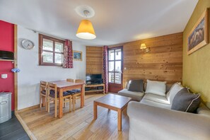 Una sala de estar con piso de madera, un sofá, un televisor, una mesa de comedor con sillas y una lámpara.