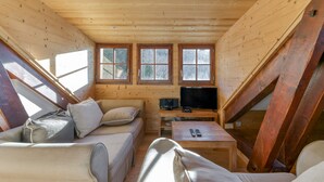 Interior acolhedor de uma cabana com teto de madeira, um sofá, uma TV e uma janela.