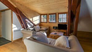 Um quarto acolhedor no estilo loft, com teto inclinado, sofá, TV e grandes janelas.
