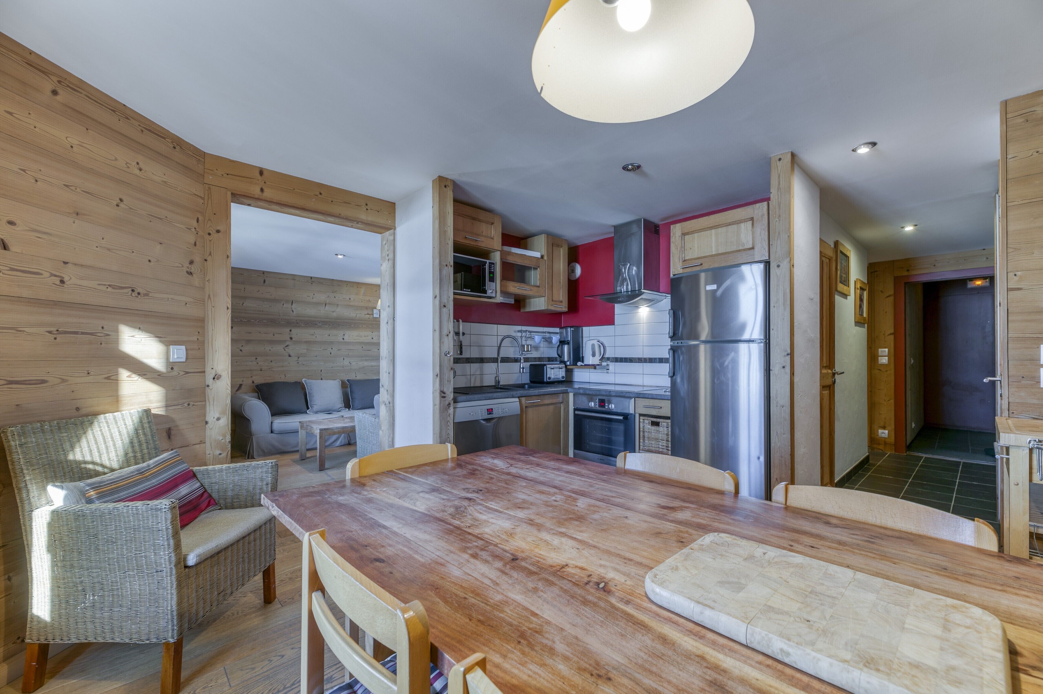 Un interior de madera con una mesa de comedor, sillas, sofá, zona de cocina con electrodomésticos y techo de madera.