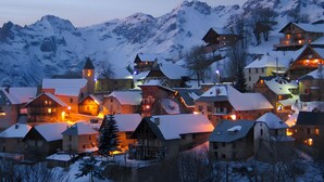 A snow-covered village with traditional wooden houses, a church tower, and a mountain backdrop. - Apartment 'Regain 6' with Mountain View and Balcony (Villard-Reculas)