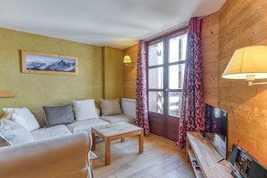Een gezellige woonkamer met een bank, een houten salontafel, een televisie en een raam met gordijnen.