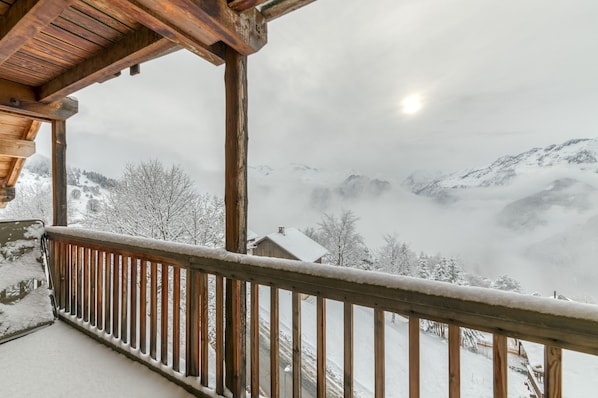 A wooden balcony with a view of snow-covered mountains and a cloudy sky.