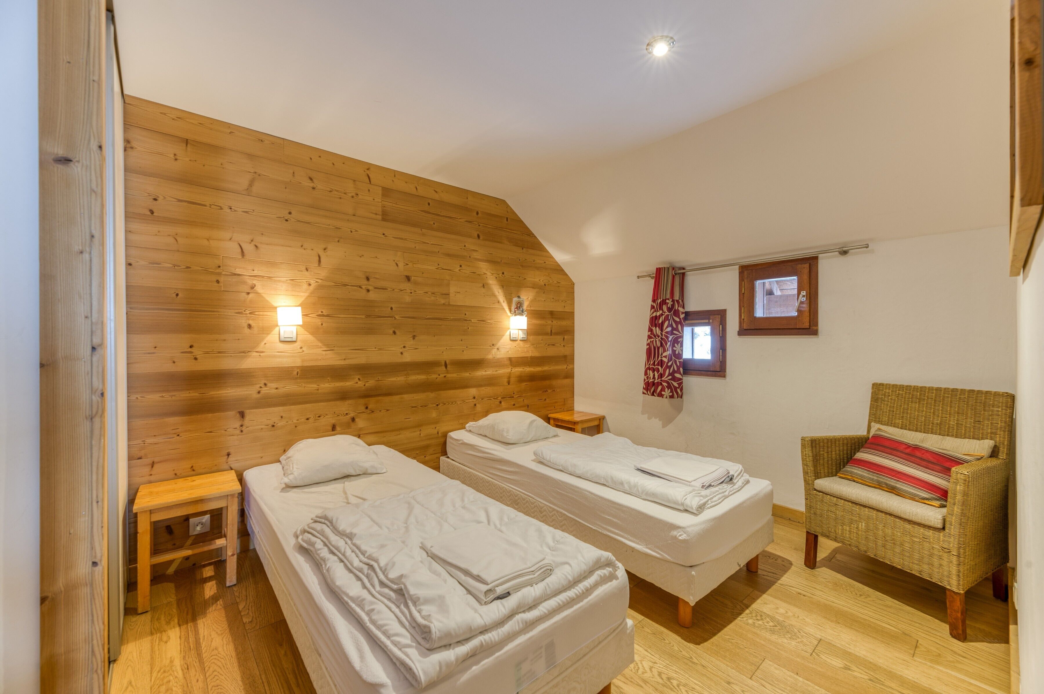 Une chambre avec deux lits, des murs en bois, une chaise en osier et une petite table.