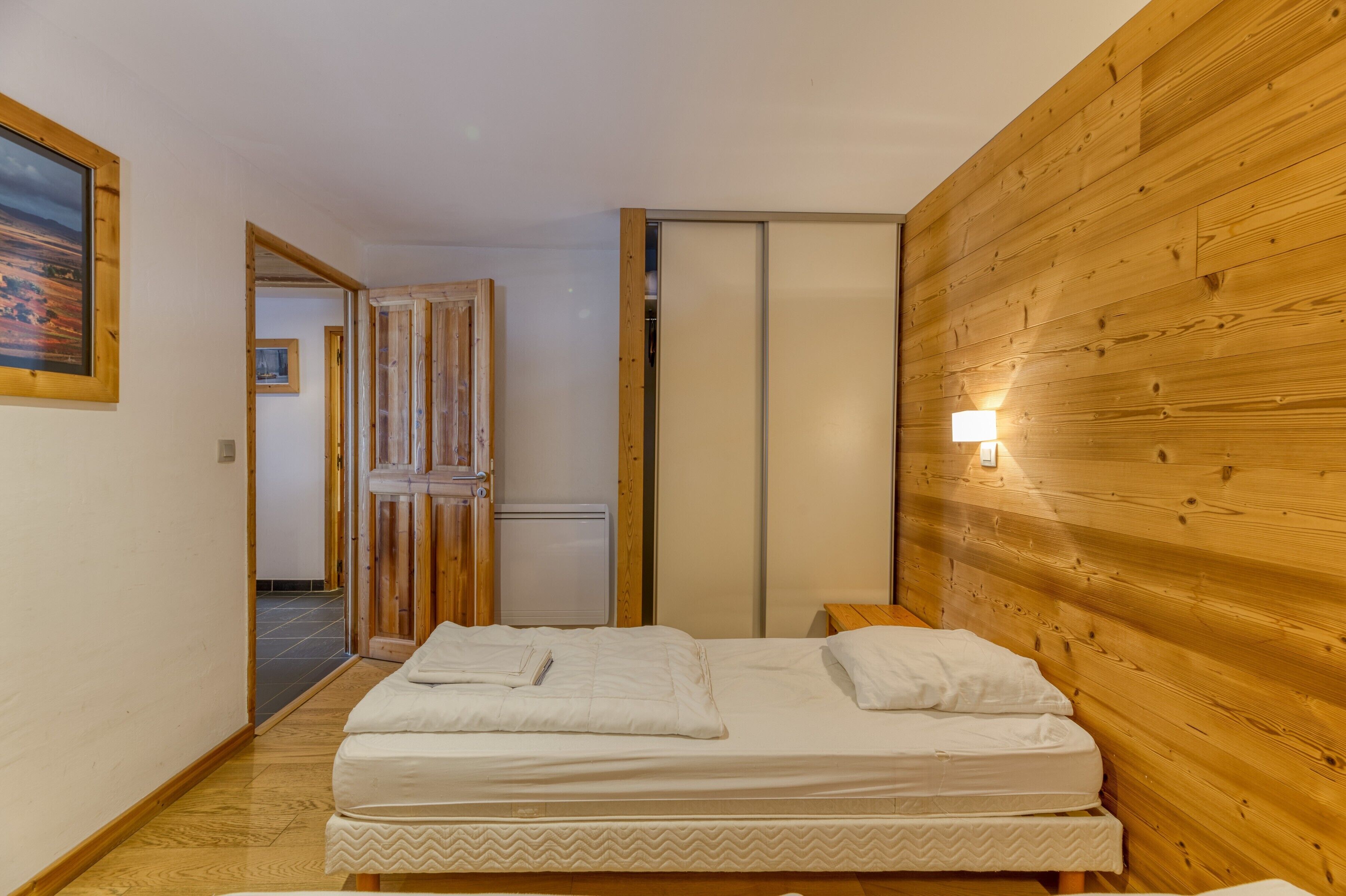 Une chambre avec un mur en bois, un lit avec une literie blanche, une table de chevet et une lampe.