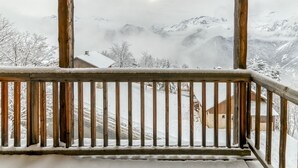 A wooden balcony with a view of snow-covered mountains and a house. - Apartment 'Regain 7' with Mountain View and Balcony (Villard-Reculas)