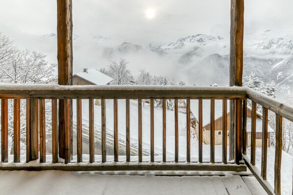 Un balcón de madera con vistas a montañas nevadas y una casa.