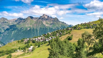 Un pueblo de montaña con casas en una ladera, rodeado de montañas y vegetación.